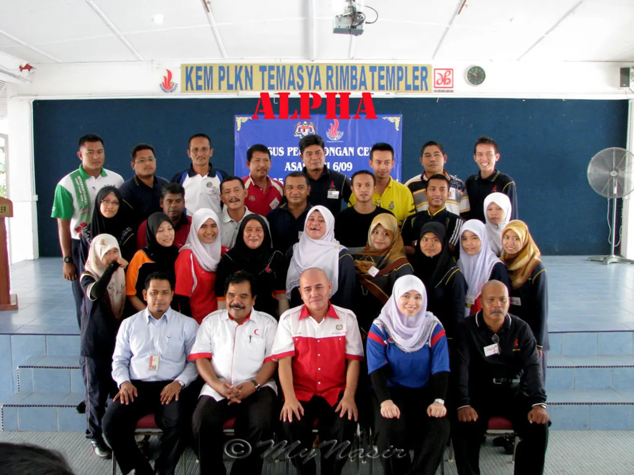 Here I can see a crowd of people smiling and giving pose for the picture. At the back of these...