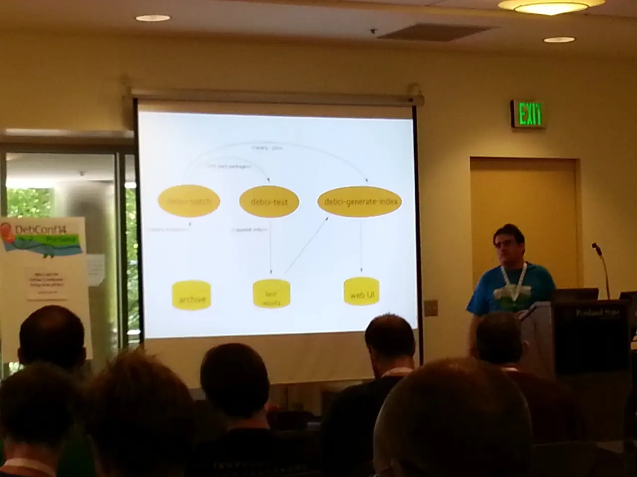 In this image we can see few persons are sitting on the chairs, a person is standing, and here is...