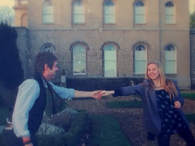 In this picture there is a couple standing on a greenery ground and holding a hand of each other...