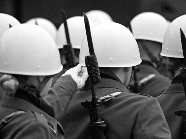 This is a black and white image. In this image I can see few people wearing uniforms, hats on their...